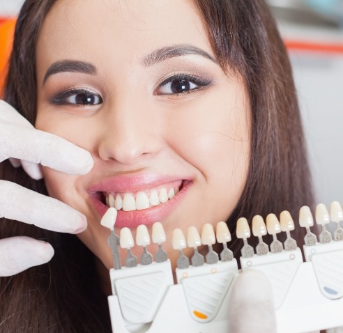 Young woman in dental chair with cosmetic dentist holding shade guide to her smile