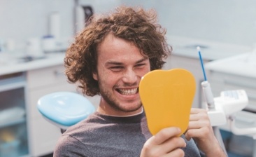 Young man in dental chair looking at his smile in a mirror
