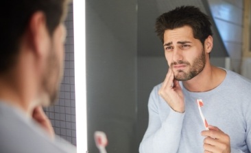 Man holding bloody toothbrush in bathroom and holding his cheek in pain