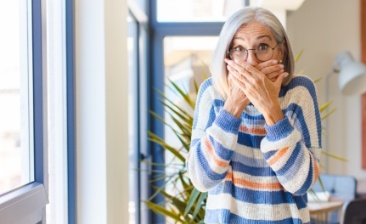 Woman with gray hair covering her mouth with both hands