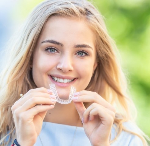 Young blonde woman smiling and holding clear aligner