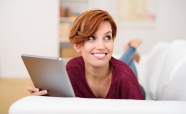 Smiling woman laying on couch and holding tablet