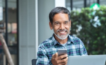 Smiling older man in blue plaid shirt holding his phone