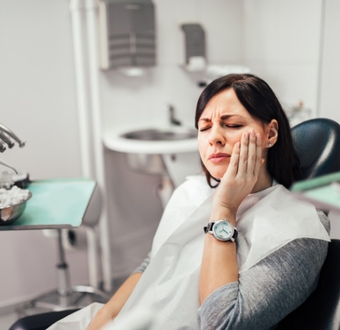 Woman holding her cheek in pain while visiting emergency dentist in Meridian