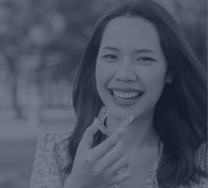 Smiling woman holding a ClearCorrect clear aligner in Meridian