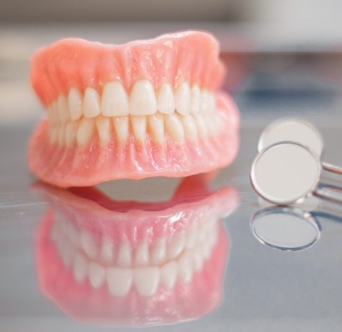 Full dentures resting on table next to two dental mirrors