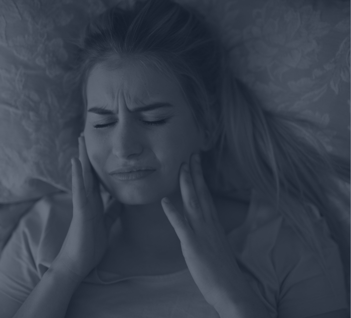 Woman lying down and holding her jaw in pain before T M J treatment in Parker