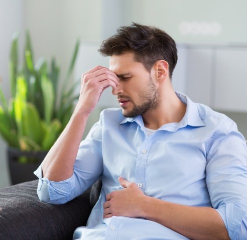 Man pinching the bridge of his nose and holding his stomach